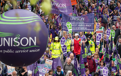 Hundreds of people marching on the streets holding UNISON flags and banners and balloons